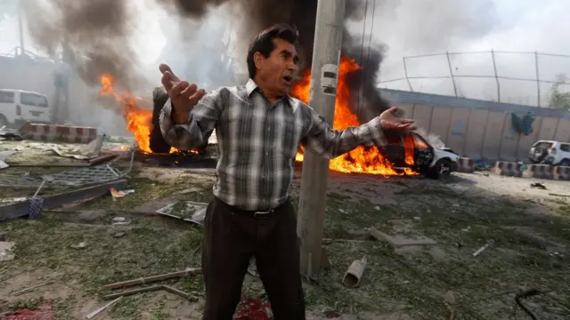 ชายคนหนึ่งยืนอยู่เบื้องหน้ารถยนต์ที่เกิดเพลิงลุกไหม้