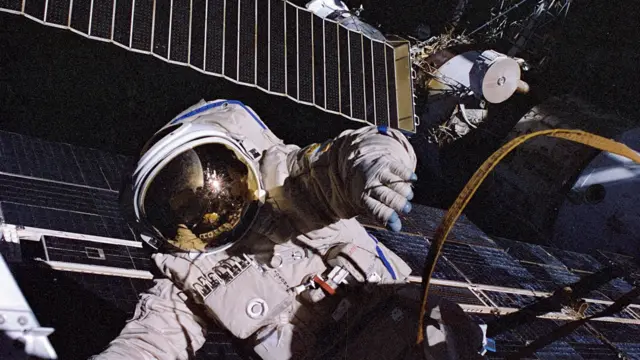 Um astronauta trabalhando no espaço, segurando uma nave espacial.