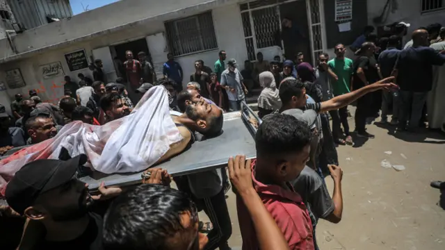  فلسطينيون يحملون جثة رجل بعد أن قُتل بالرصاص في نقطة توزيع طعام بمستشفى الشفاء في مدينة غزة، 20 يوليو/تموز 2025. 