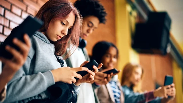 Jovens, lado a lado, usando celulares