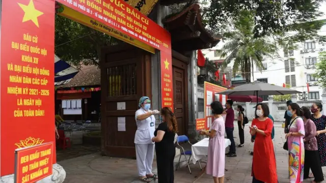 Người xếp hàng để kiểm tra nhiệt độ trước khi bỏ phiếu tại một điểm bỏ phiếu ở Hà Nội vào ngày 23 tháng 5 năm 2021