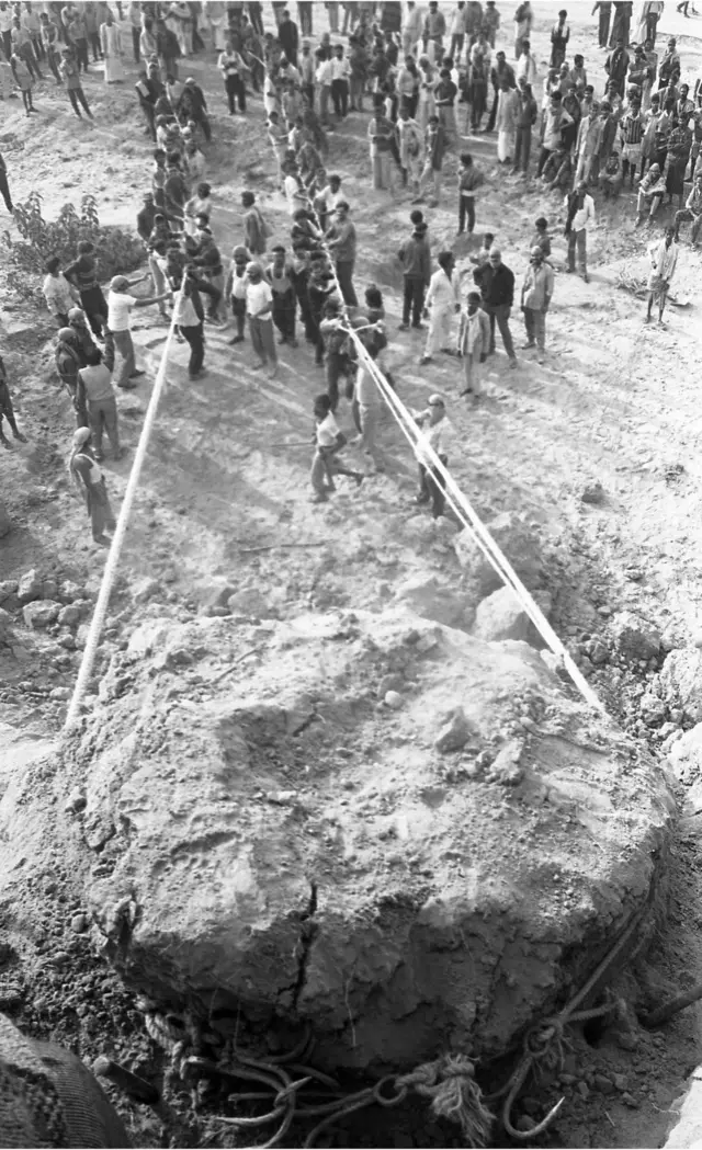 માટીના મોટા ઢગલાને ગબડાવવાનો પ્રયાસ કરતા લોકો