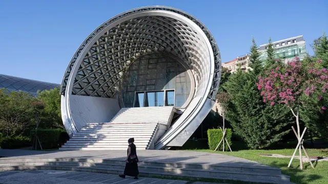 Женщина проходит у здания «кувшинов Рике» в Тбилиси. 2025 год 