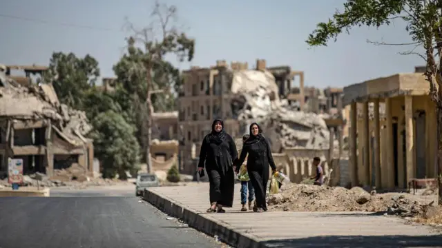 Women walk past destroyed buildings in the northern Syrian city of Raqa, the former Syrian capital of the Islamic State (IS) group, on August 21, 2019