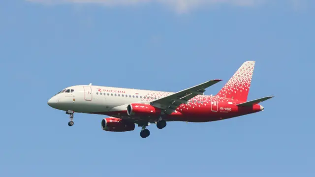 سفید اور سرخ رنگ کا روسیا سخوئی سپر جیٹ 100 روس کے شہر سینٹ پیٹرز برگ کے پلکووو ائیرپورٹ پر اترنے کی تیاری کر رہا ہے