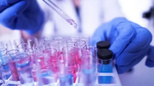 Las manos con guantes de un investigador colocando muestras en unas probetas