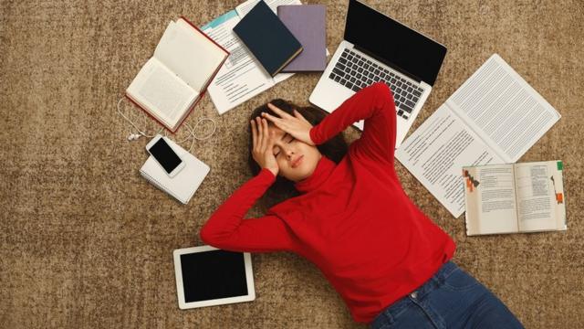 Una joven cansada en el piso con los libros y computadora.