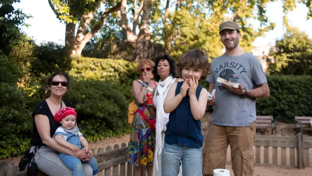 Žena sa detetom na krilu, u sredini dečak, iza njega muškarac sa kačketom, a u daljini dve žene