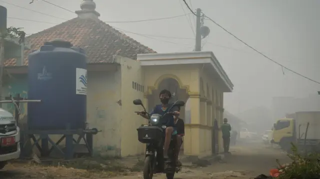 Seorang anak memakai masker saat melintasi jalan yang diselimuti kabut asap kebakaran Tempat Pembuangan Akhir (TPA) Jatiwaringin di Rajeg, Kabupaten Tangerang, Banten, Jumat (3/7/2026).