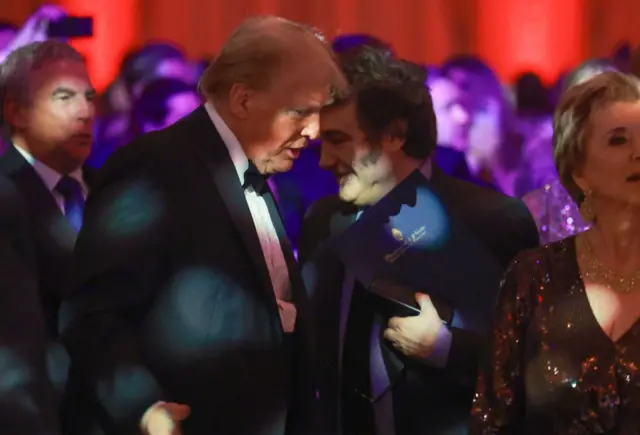 Trump e Milei vestidos com traje de gala e conversando bem próximos