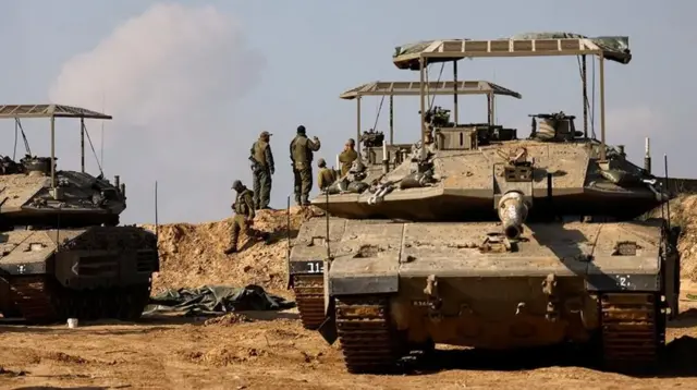 جنگ بندی کے بعد اسرائیلی فوجی ٹینکو کے قریب جمع ہوئے ہیں جبکہ ان کے پیچے غزہ کے ابھرتا دھواں ہے