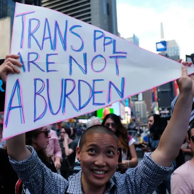Manifestante con cartel que dice: "Las personas transgénero no son una carga".