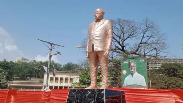 Front view of di statue of Nana Akufo-Addo, wey dey in bronze colour. E dey wear suit, glasses and e dey smile. E dey outside Effia-Nkwanta Regional Hospital for Sekondi, Ghana - November 2024