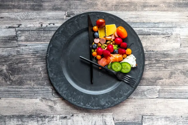 Un plato con algo de comida y los cubiertos colocados como si fueran las agujas del reloj.