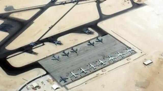 Em uma imagem aérea da base aérea de Al-Udeid, uma série de aviões é vista na pista, que é cercada pelo deserto.
