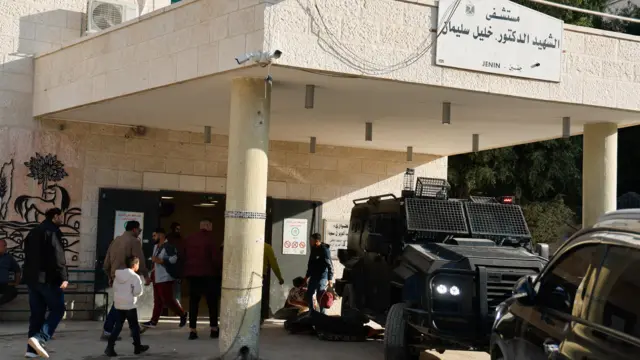 أشخاص يسيرون بجوار مركبة لقوات الأمن الفلسطينية في جنين بالضفة الغربية المحتلة