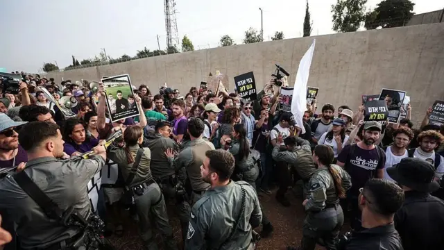 متظاهرون مناهضون للحرب يحملون صور أطفال فلسطينيين قُتلوا في العمليات العسكرية الإسرائيلية في غزة. أمامهم جنود إسرائيليون يحاولون منعهم من التقدم. الصورة التقطت نهاراً.
