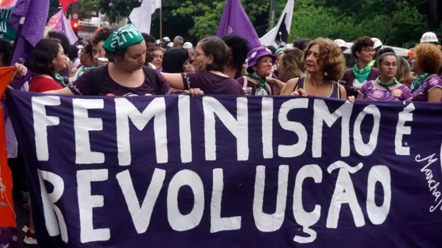 Mulheres durante manifestação segurando uma faixa "Feminismo é revolução"