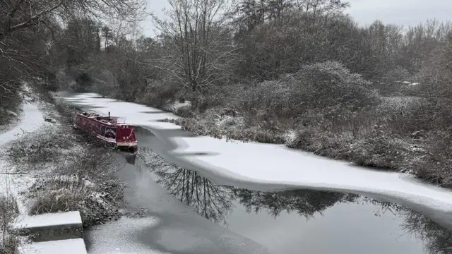 Un canal con una barcaza tras una nevada. Partes del agua están cubiertas de nieve y hielo.