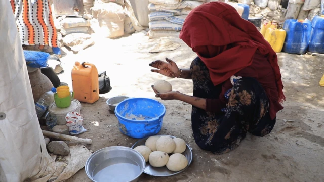 امرأة في مخيم لللاجئين في تعز جاثية على الأرض تعد خبزا