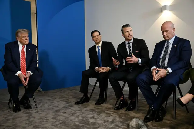 Trump, Dışişleri Bakanı Marco Rubio ile ABD Savunma Bakanı Paul Hegseth'ın yanında oturuyor. Önüne bakıyor. Hegseth gazeteciye bakarak soruya yanıt veriyor.
