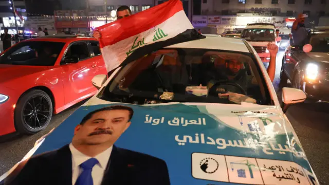 رجل يحمل علم العراق من سيارة عليها ملصق انتخابي يظهر رئيس الوزراء الحالي محمد شياع السوداني، بينما يحتفل أنصار ائتلاف إعادة الإعمار والتنمية بعد الإعلان عن النتائج الأولية للانتخابات في بغداد، العراق، 12 نوفمبر/تشرين الثاني 2025.
