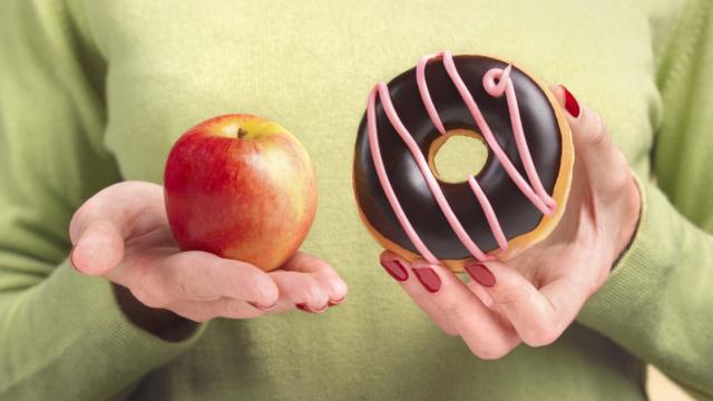 Mulher segurando maçãaposta para jogo do brasiluma mão e um donut na outra