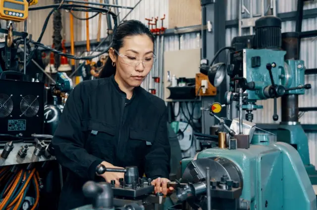 امرأة تستخدم معدات التصنيع في ورشة تصنيع المعادن في اليابان.