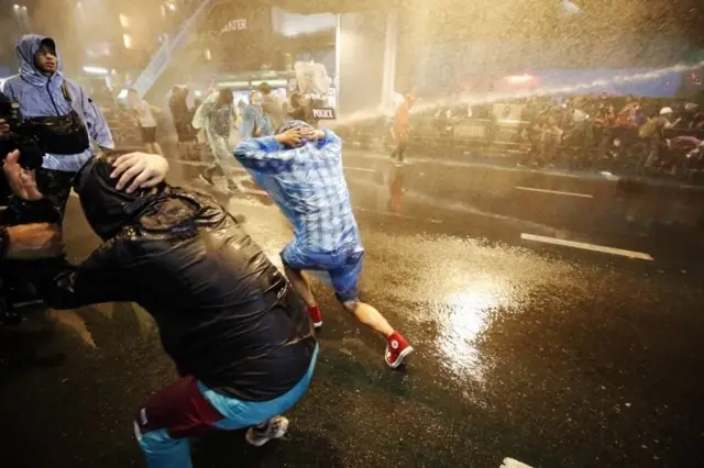 Pro-democracy protesters react as riot police fire water canons during an anti-government protest in Bangkok, Thailand, 16 October 2020
