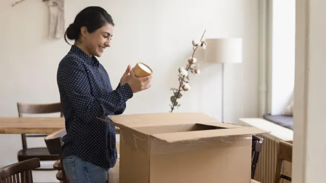 Salonda bir masanın yanında ayakta dururken kargosunu açan bir kadın