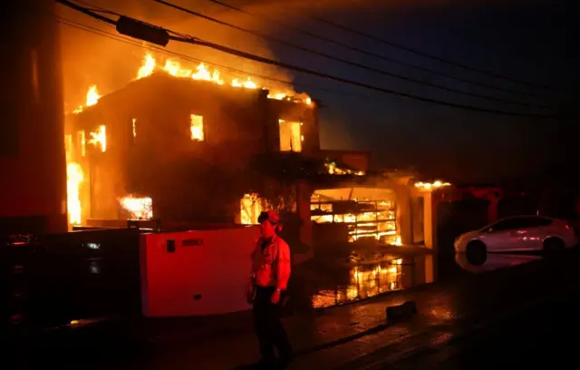 आग की चपेट में आए एक घर के आगे खड़ा अग्निशमन कर्मी