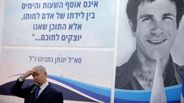 Benjamin Netanyahu discursa diantef12 bet como apostarum cartaz com a imagemf12 bet como apostarseu falecido irmão, Yonatan, durante cerimôniaf12 bet como apostarhomenagem a ele
