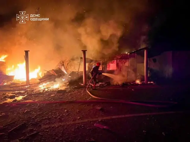 Пожежа на території прикордонного об’єкта після удару: рятувальник гасить вогонь, навколо – уламки та пошкоджені конструкції, у повітрі густий дим.