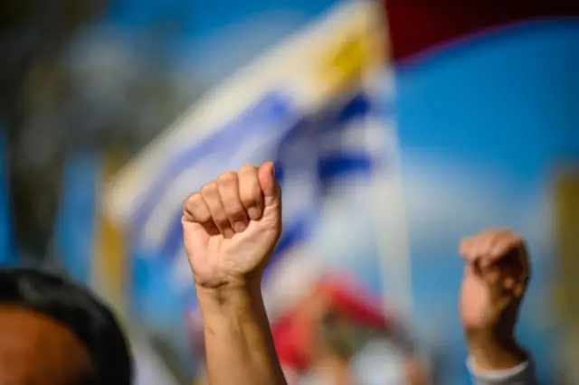 Puño en alto con bandera de Uruguay detrás.