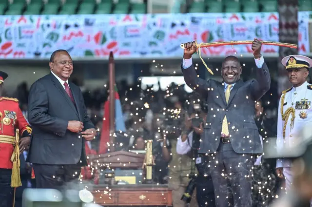 President Uhuru Kenyatta looks on as President William Ruto lifts a sword