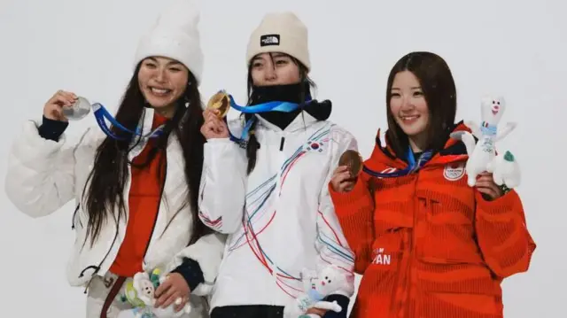 3人が首からかけたメダルを右手で持ちながら横並びに立っている。小野とキムは笑顔、チェは口元がカバーで見えない。全員、左手には大会マスコットのぬいぐるみを持っている