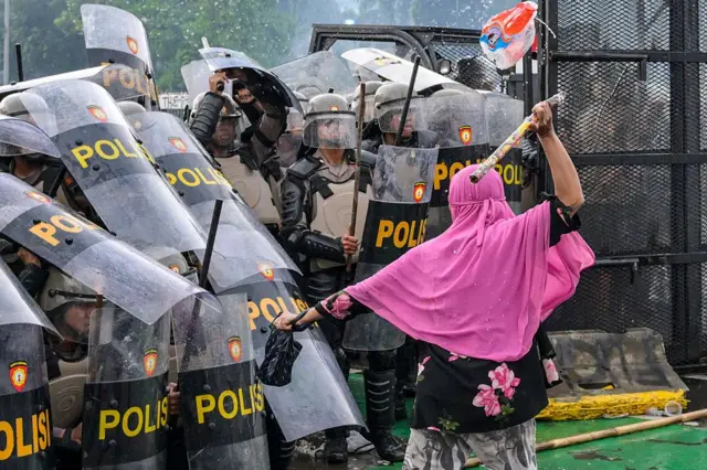 A woman strikes a police officer with a bamboo stick as police push back students during a protest outside the parliament building against lawmakers' demands for higher allowances in Jakarta on August 28, 2025. (Photo by BAY ISMOYO / AFP) (Photo by BAY ISMOYO/AFP via Getty Images)