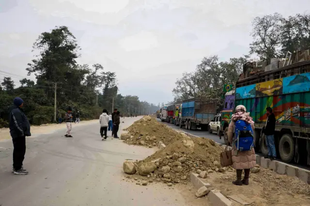 दाउन्ने क्षेत्रमा सडक अवरुद्ध भएपछि राजमार्गमा अलपत्र परेका सवारीसाधन र सडकको छेउमा उभिएका केही यात्रुहरू