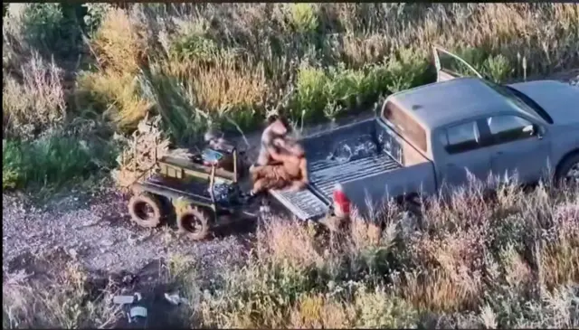 Чоловік переладає пораненого військового в кузов пікапа