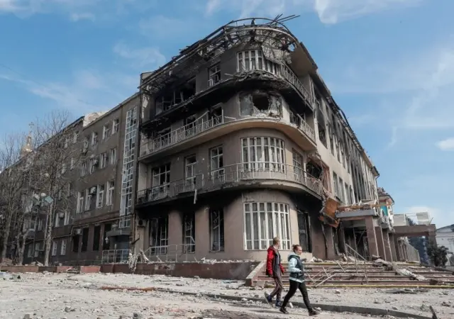 Residents walk near a building destroyed in the course of the Ukraine-Russia conflict, in the southern port city of Mariupol, Ukraine April 10, 2022.