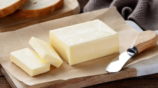 Sliced pieces of butter on a cutting board, wooden background. Piece of butter.

පෙති කපන ලද බටර් කැබලි.
