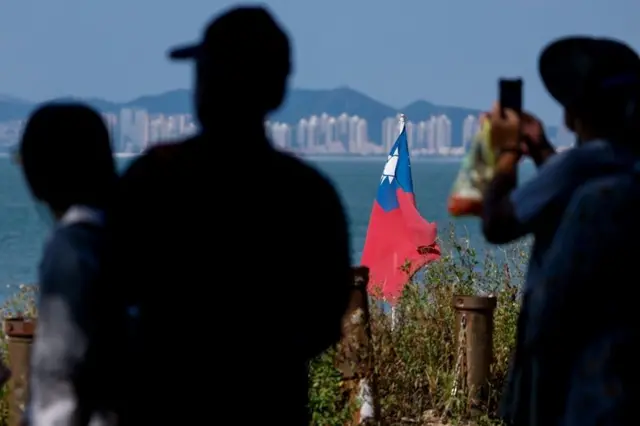 Tourists take photos as a Taiwan flag flies, with China's Xiamen in the background, on Dadan Island, in Kinmen, Taiwan, October 18, 2025. REUTERS/Ann Wang