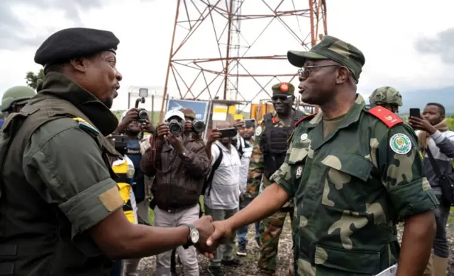 Willy Ngoma (ibumoso) aramukanya na Brigadier General Emmanuel Kaputa (iburyo) w'ingabo za FARDC imbere y'abanyamakuru benshi barimo kubafotora