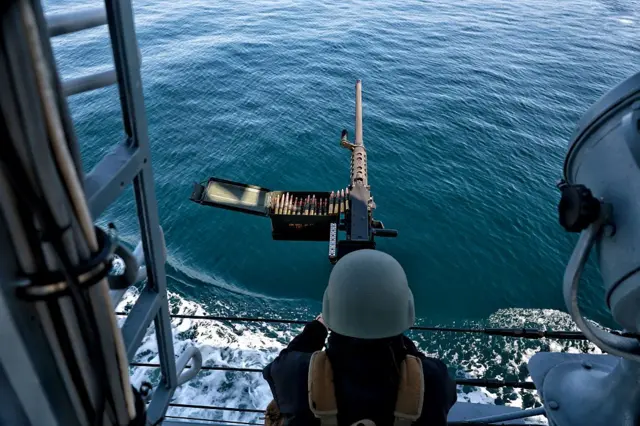 Marynarz ukraińskiej marynarki wojennej stoi przy karabinie maszynowym na pokładzie statku podczas patrolu na Morzu Czarnym wzdłuż wybrzeża Odessy, Ukraina