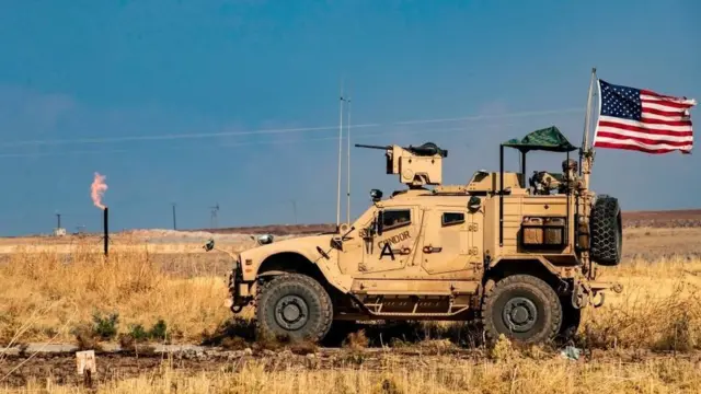 US armoured vehicle drives past a burning gas flare in north-eastern Syria