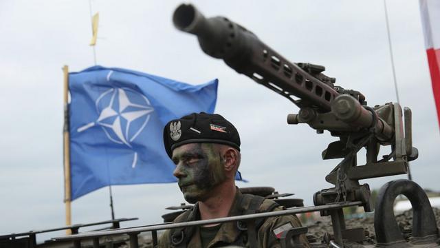 Soldado con la bandera de la OTAN atrás.