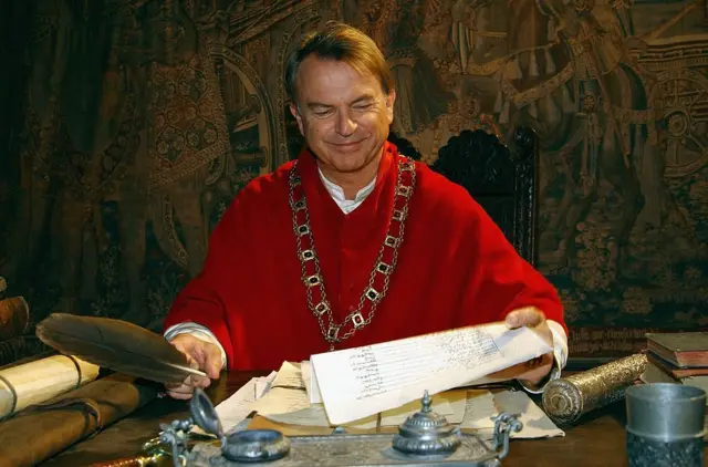 Сем Нілл в біло червоному одязі кардинала