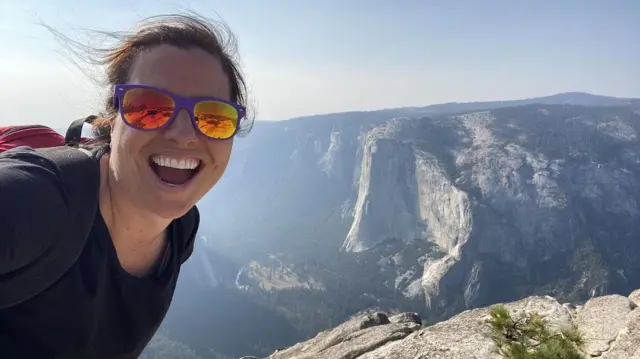 A advogada americana Jamie, que usa o pseudônimo M. E. Thomas, uma mulher branca jovembarcelona atletico madridóculos escuros espelhados, numa selfie sorrindobarcelona atletico madriduma paisagem montanhosa