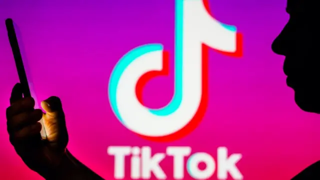 Sur cette photo d'illustration, la silhouette d'une femme tient un smartphone avec le logo TikTok en arrière-plan.