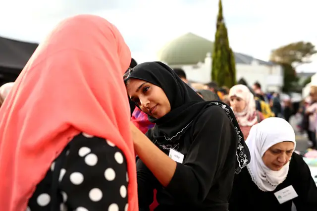 یک زن مسلمان در حال کمک به یکی از شرکت‌کنندگان برای گذاشتن حجاب در شهر اوکلند در مراسم یادبود کشته‌شدگان کرایست‌چرچ، نیوزیلند